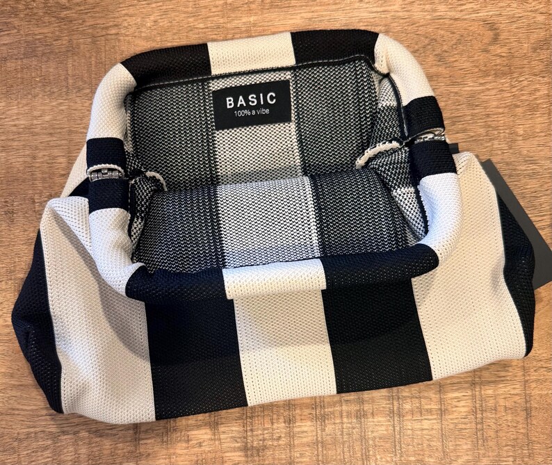 May include: A black and white striped handbag with a rectangular shape. The bag has a handle and a label that reads "BASIC 100% a vibe". The bag is made of a woven material.