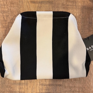 May include: A black and white striped clutch bag with a tag that reads "BASIC 100% a vibe". The bag has a rectangular shape with rounded edges. The stripes are vertical and alternate between black and white.