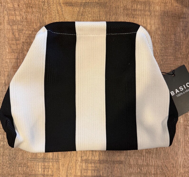 May include: A black and white striped clutch bag with a tag that reads "BASIC 100% a vibe". The bag has a rectangular shape with rounded edges. The stripes are vertical and alternate between black and white.