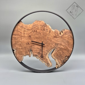 May include: A circular wall clock with a natural wood face and a black metal frame. The clock face displays Roman numerals and black hands. The wood grain is visible, and the clock has an irregular shape. The clock is approximately 30 cm in diameter.