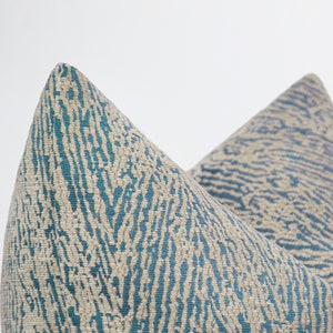 May include: Two throw pillows with a teal and beige abstract pattern. The pillows are made of a soft, textured fabric.