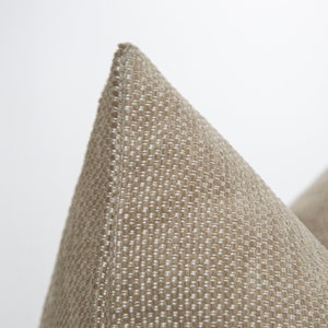 Peut inclure: Gros plan sur le coin d'un coussin beige avec un tissu texturé. Le tissu présente un motif tissé subtil avec une nuance de beige légèrement plus claire.