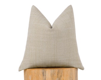 May include: A beige throw pillow with a subtle textured fabric. The pillow is sitting on a wooden stump.
