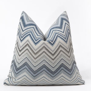 Könnte beinhalten: Ein blaues und graues Kissen mit Chevron-Muster. Das Kissen ist aus einem weichen, strukturierten Stoff.