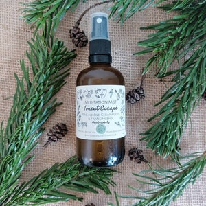 May include: A brown glass bottle with a spray nozzle, filled with a clear liquid. The bottle has a white label with the text "Meditation Mist Forest Escape Pine Needle, Cedarwood & Frankincense Handmade by www.kogandbellflower.co.uk"