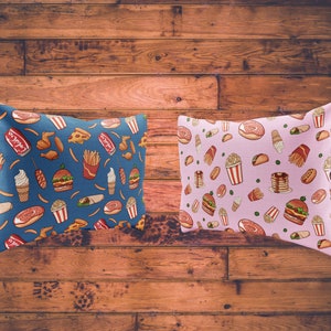 May include: Two decorative throw pillows with a blue and pink background. The pillows feature a repeating pattern of fast food items like burgers, fries, donuts, and ice cream cones.