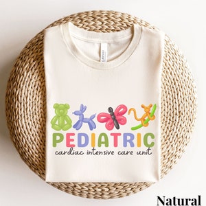 May include: A natural colored t-shirt with a graphic of balloon animals and the text "PEDIATRIC cardiac intensive care unit".
