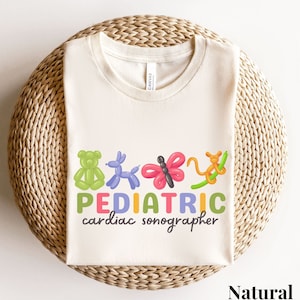 May include: A natural colored t-shirt with a graphic of colorful balloon animals and the text "PEDIATRIC cardiac sonographer".