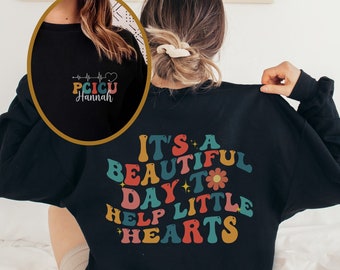 May include: Black sweatshirt with a colorful retro design that says "It's a beautiful day to help little hearts". The back of the sweatshirt has a white design with a heartbeat and the text "PICU Hannah".