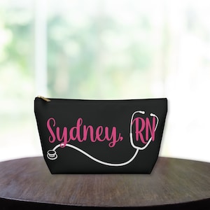 May include: Black zippered makeup bag with a white stethoscope design and the text "Sydney, RN" in pink lettering.