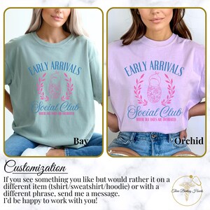Op de afbeelding: Twee T-shirts met een grafisch ontwerp met een babypop met een bloemenpatroon en de tekst "Early Arrivals Social Club Where Due Dates Are Overrated". De T-shirts zijn in de kleuren bay en orchid.