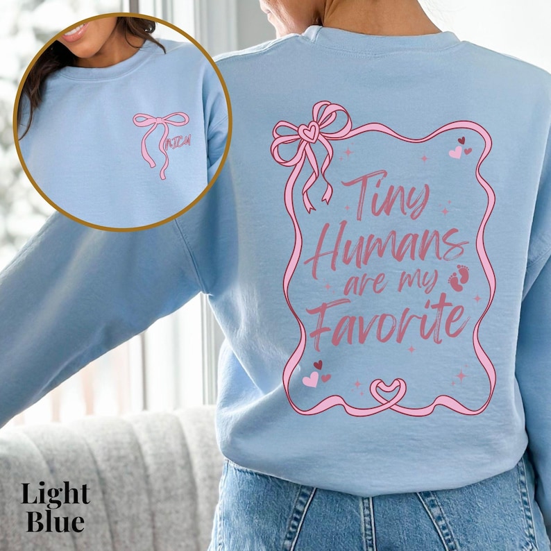 May include: Light blue sweatshirt with a pink ribbon and the text "Tiny Humans are my Favorite" in a pink frame.