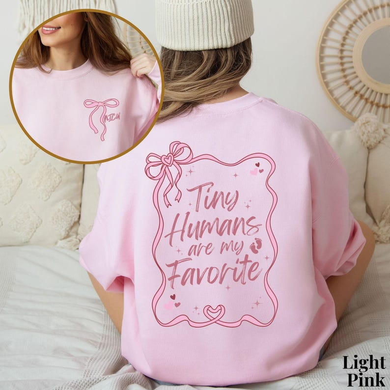 May include: Light pink sweatshirt with a pink graphic that says "Tiny Humans are my Favorite" with a pink bow and baby footprints.