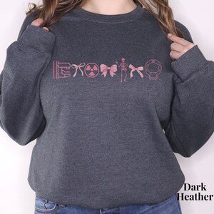 May include: Dark heather grey sweatshirt with a pink graphic of medical symbols including a stethoscope, a radiation symbol, a bow, a skeleton, and a CT scan.