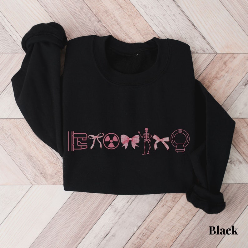 May include: Black sweatshirt with a pink graphic of medical symbols and a skeleton wearing a bow. The symbols include a stethoscope, a radiation symbol, a bow, and an MRI machine.