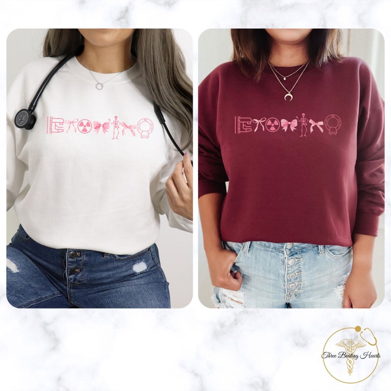 May include: Two women wearing pink and white sweatshirts with a pink graphic of medical symbols. The sweatshirts are a light pink and a maroon color. The women are wearing blue jeans.