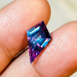 Könnte beinhalten: Ein drachenförmiger Edelstein mit Facettenschliff, der einen Farbverlauf von tiefem Violett über Magenta bis hin zu leuchtendem Cyanblau aufweist. Der Stein hat eine scharfe, geometrische Silhouette mit mehreren dreieckigen Facetten.