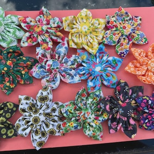 Peut inclure: Une collection de fleurs décoratives en tissu aux motifs variés, notamment floraux et de tournesols. Les fleurs sont disposées sur une surface rose, présentant une variété de couleurs et de styles.