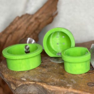 May include: Three bright green, circular objects with a rim, possibly coasters or small containers, are arranged on a wooden surface. One has a suction cup attached. The objects are a vibrant, solid green colour.