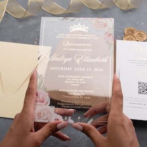 May include: Clear acrylic Quinceañera invitation with floral design and gold accents. The invitation includes the name "Nadiya Elizabeth" and event details. A cream-colored envelope and additional cards are also visible.