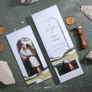 May include: Wedding invitation suite featuring a photo of a couple kissing, with the text "The Wedding of Ashley and Gabriel." Includes gold wax seals, a wooden stamp, and decorative stone pieces. The invitation has a landscape design.