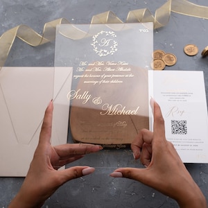 May include: Clear acrylic wedding invitation with gold accents. The invitation features elegant script with the names "Sally & Michael" and event details. Includes a matching envelope, RSVP card, and gold wax seals.
