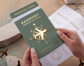 Può includere: Un invito di nozze verde a forma di passaporto con scritte dorate e un design a bussola aereo dorato. L'invito recita "Wedding Pass" e "Wedding Invitation". Anche i nomi "Ashley & Gabriel" sono stampati.