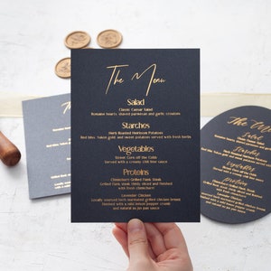 Könnte beinhalten: Eine schwarze Karte mit goldenen Lettern listet ein Menü für eine Hochzeit oder ein Event auf. Das Menü umfasst Salat, Stärke, Gemüse und Proteine. Der Text "The Menu" ist oben auf der Karte in Kursivschrift geschrieben.