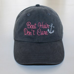 May include: A dark blue baseball cap with the text "Boat Hair Don't Care" embroidered in pink with a silver anchor.