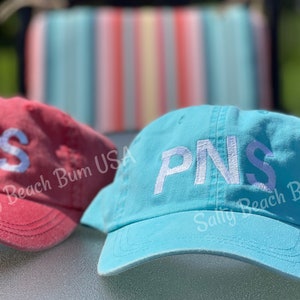 May include: Two embroidered baseball caps with the letters "PNS" in white on a red and a blue cap. The caps have the text "Salty Beach Bum USA" on the side.