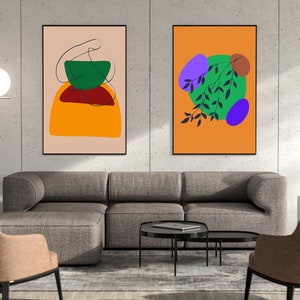 May include: Two framed abstract art prints with geometric shapes and colors. The print on the left features a green, red, and orange design. The print on the right features a green, purple, and orange design with a black branch.
