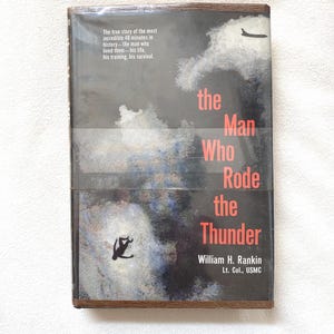 May include: A hardcover book titled The Man Who Rode the Thunder by William H. Rankin, Lt. Col., USMC. The dark cover features a silhouette of a falling person, a small airplane, and white clouds. Text reads: The true story of the most incredible 40 minutes in history—the man who lived them—his life, his training, his survival.