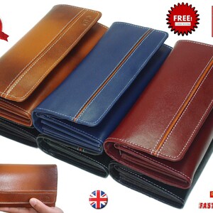 May include: Four leather wallets in different colours: brown, blue, burgundy, and black. Each wallet has a stitched design and a small logo on the front. The wallets are arranged in a stack, with the brown wallet on top.