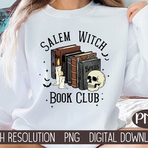 K&ouml;nnte beinhalten: Wei&szlig;es Sweatshirt mit einem grafischen Design aus einem Stapel B&uuml;cher mit einem Sch&auml;del und Kerzen. Der Text "Salem Witch Book Club" ist auf dem Sweatshirt aufgedruckt.