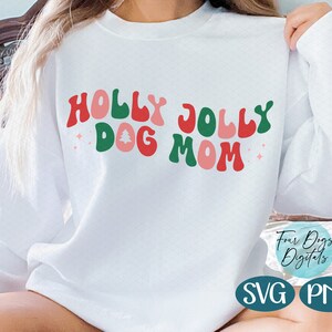 May include: White sweatshirt with the text "Holly Jolly Dog Mom" in red, green, and pink retro-style lettering. The text includes a small pink Christmas tree graphic.