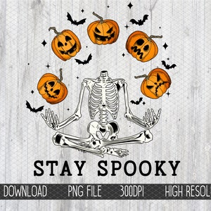 May include: A skeleton in a yoga pose with the text "STAY SPOOKY" below. The skeleton is surrounded by six orange jack-o'-lantern pumpkins and black bats.