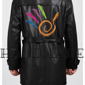 Pu&ograve; includere: Trench in pelle nera con un design colorato sul retro. Il design presenta un vortice e linee in rosa, blu, verde e arancione. Il cappotto ha una cintura e la parola "HANDMADE" &egrave; stampata in basso.