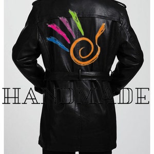 Pu&ograve; includere: Trench in pelle nera con un design astratto colorato sul retro. Il cappotto ha una cintura e un colletto. Il testo "HANDMADE" &egrave; stampato sotto il cappotto.
