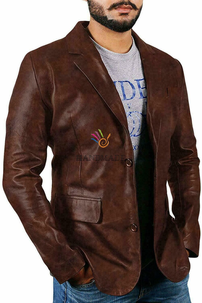 May include: A brown leather blazer with a single button closure. The blazer has a pocket on the left side and a small logo on the right side that says "HANDMADE".