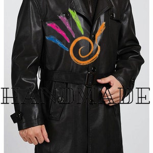 Pu&ograve; includere: Un trench in pelle nera con cintura e chiusura a doppio petto. Il cappotto ha un colletto e due tasche sul davanti. Il testo "HANDMADE" &egrave; visibile nella parte inferiore dell'immagine.