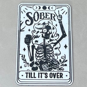 May include: A rectangular sticker with a black and white illustration of a skeleton with long hair, holding a fist and pointing up. The text "SOBER" is at the top, and "TILL IT'S OVER" is at the bottom.