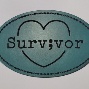 May include: Teal oval leather patch with the word "Survivor" in black letters, a semicolon, and a heart shape. The patch has a stitched border.