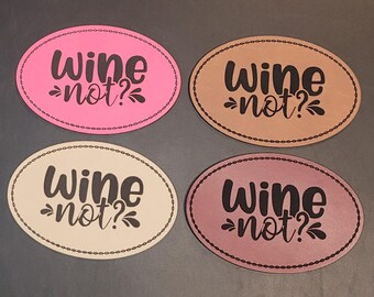 May include: Four oval-shaped coasters in pink, tan, cream, and mauve. Each coaster has the phrase "Wine not?" in black script. The coasters have a decorative dotted border.