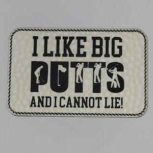 May include: Rectangular golf-themed sign with the text "I LIKE BIG PUTTS AND I CANNOT LIE!" in black. The sign has a textured, off-white background and a black rope-like border. Golfing figures are incorporated into the word "PUTTS".