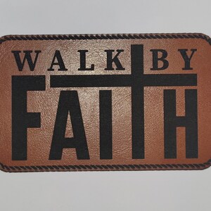 May include: A rectangular brown patch with the words "WALK BY FAITH" in bold black letters. A black cross is centered between the words. The patch has a decorative rope-like border.