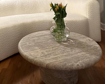 May include: A white, curved sofa with a gray stone coffee table. A glass vase with yellow and orange tulips sits on the table.