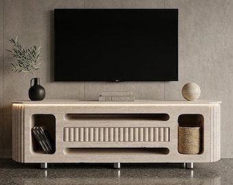 Könnte beinhalten: Ein moderner, hellfarbiger TV-Schrank mit integrierter Beleuchtung und offenem Stauraum. Der Schrank hat eine strukturierte Front und einen schwarzen Fernseher darüber. Es gibt eine schwarze Vase, eine dekorative Kugel und einen kleinen Korb.