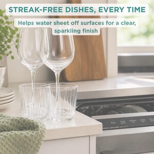 May include: Two clear wine glasses and two clear ribbed drinking glasses sit on a counter. Text reads: STREAK-FREE DISHES, EVERY TIME. Helps water sheet off surfaces for a clear, sparkling finish. A dishwasher control panel is visible nearby.