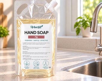 Könnte beinhalten: Ein 1L Nachfüllbeutel aus transparentem Kunststoff mit Arborfill Handseife im Duft Feige. Das Etikett enthält den Markennamen, die Produktbezeichnung, Inhaltsstoffe und drei kreisförmige Symbole für natürliche Inhaltsstoffe.
