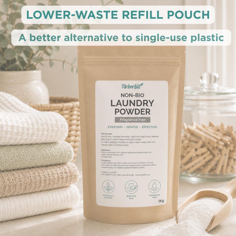 K&ouml;nnte beinhalten: Ein brauner Nachf&uuml;llbeutel aus Papier mit Arbortill Non-Bio-Waschpulver, 1kg, und einem wei&szlig;en Etikett mit dem Text "LOWER-WASTE REFILL POUCH" und "A better alternative to single-use plastic." Der Beutel steht neben einem Stapel gefalteter Handt&uuml;cher.